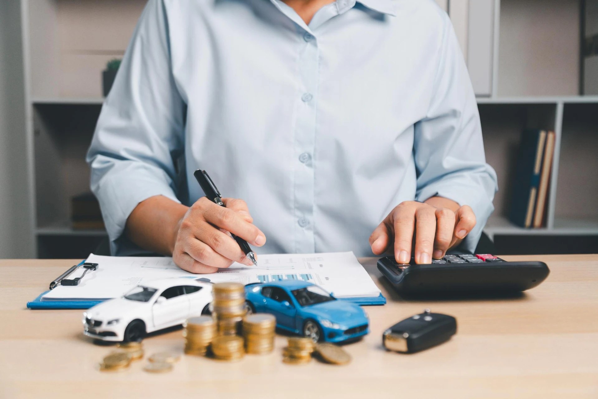 Consultor fazendo o planejamento financeiro da compra de um carro, com calculadora, moedas e miniaturas sobre a mesa